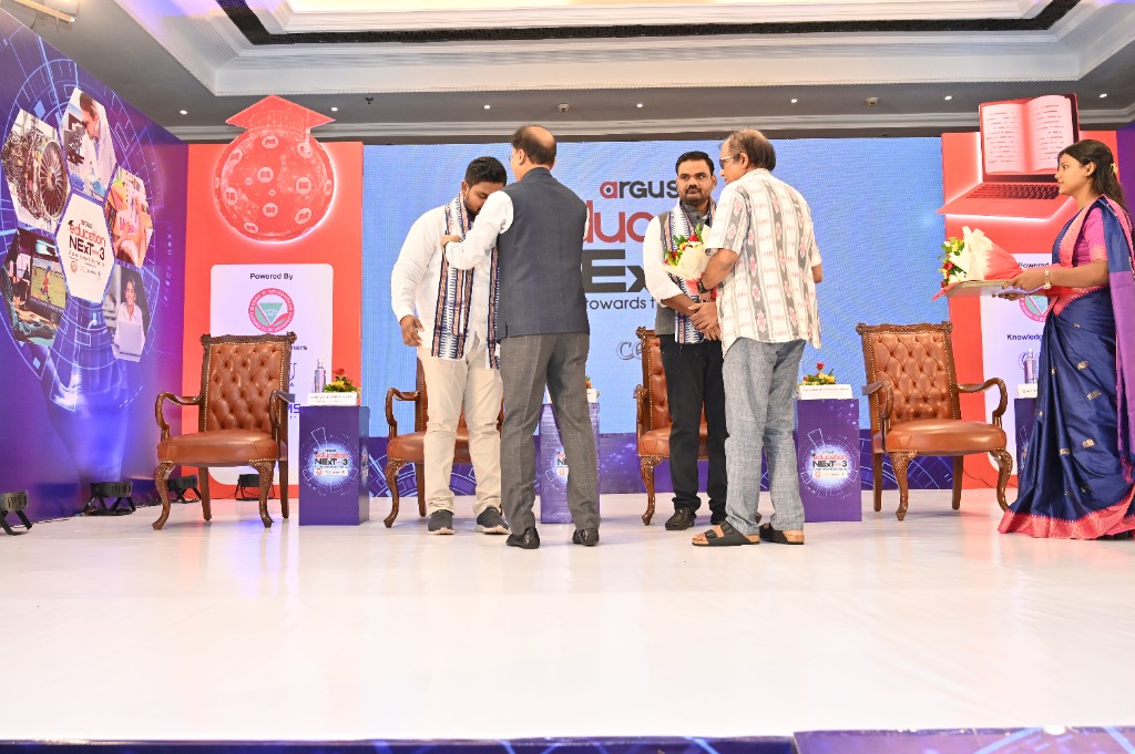 Felicitation on stage with ceremonial stole and Argus Education Next branding